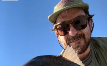 915 | How a Music Producer Built a Fly Fishing Podcast from Scratch with Pablo Signori Pablo Signori holding a large fish while fly fishing near a coastal city