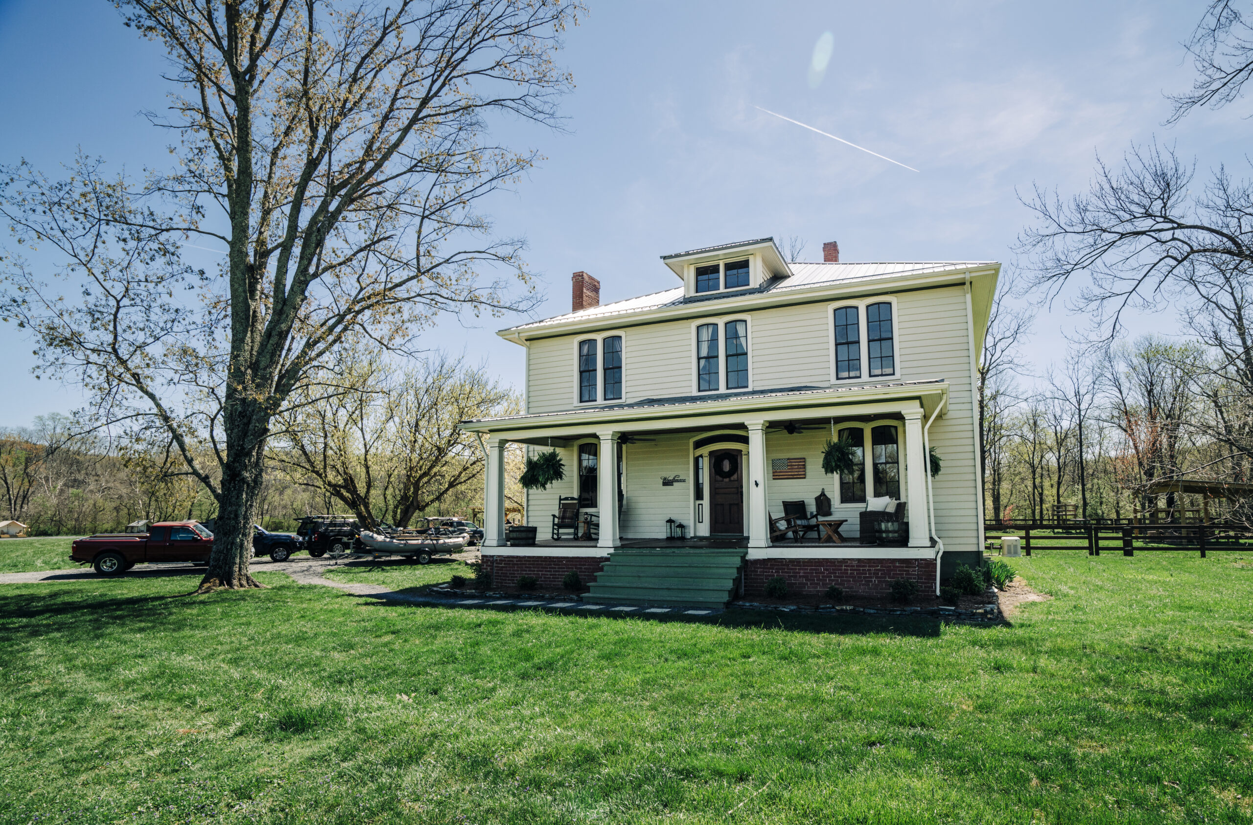 Historic white two-story fly fishing lodge with green porch steps and rocking chairs, set against a clear blue sky in Eagle Rock, Virginia.