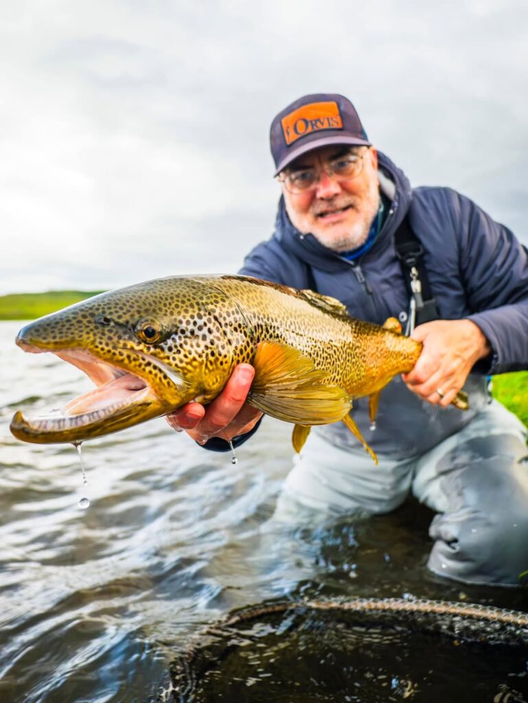 Fly angler holding a brown trout in shallow water, showing that finding fish takes practice
