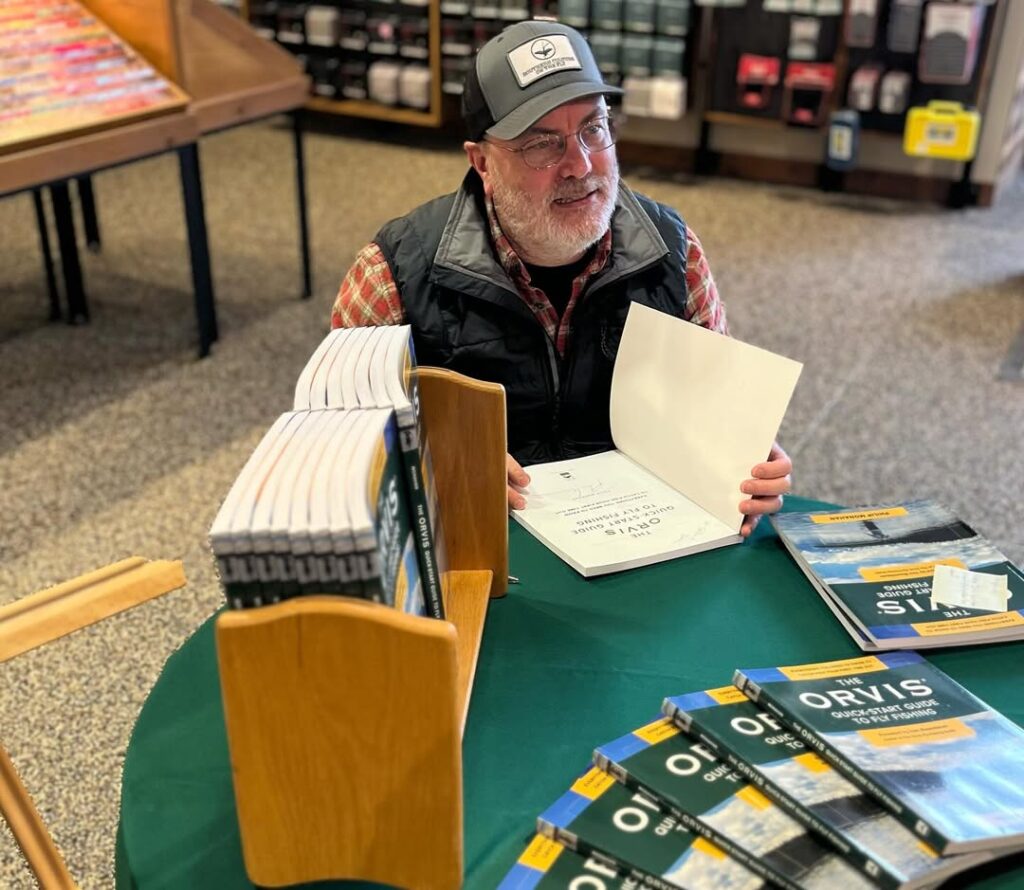 Phil Monahan signing fly fishing books at an event, sharing his approach to simplifying fly fishing