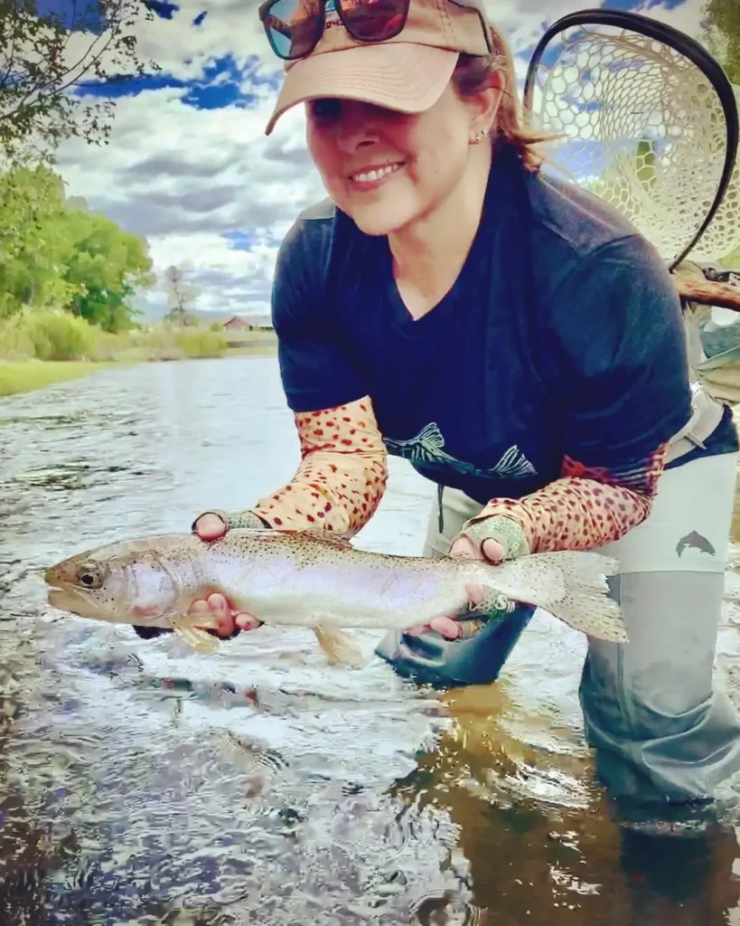 Trisha Valdez holding a trout while fly fishing New Mexico in a small river