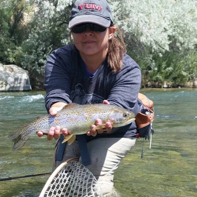 Trisha Valdez fly fishing New Mexico holding a brown trout in a clear mountain river