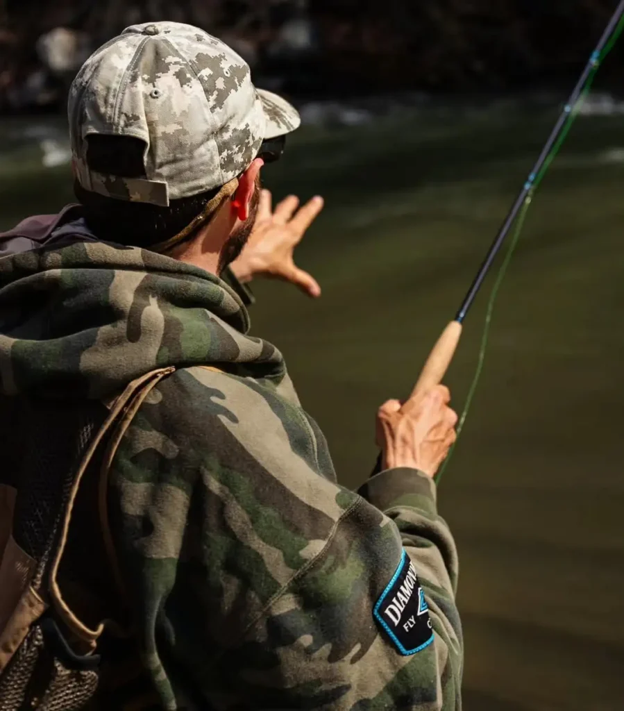 Fly angler pointing to a river seam while explaining trout holding water and structure like drop-offs and undercut banks.