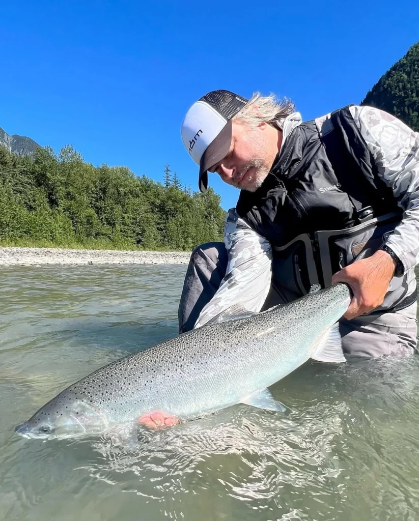 Dax Messett landing a wild steelhead while fly fishing on a Pacific Northwest river during winter steelhead season.