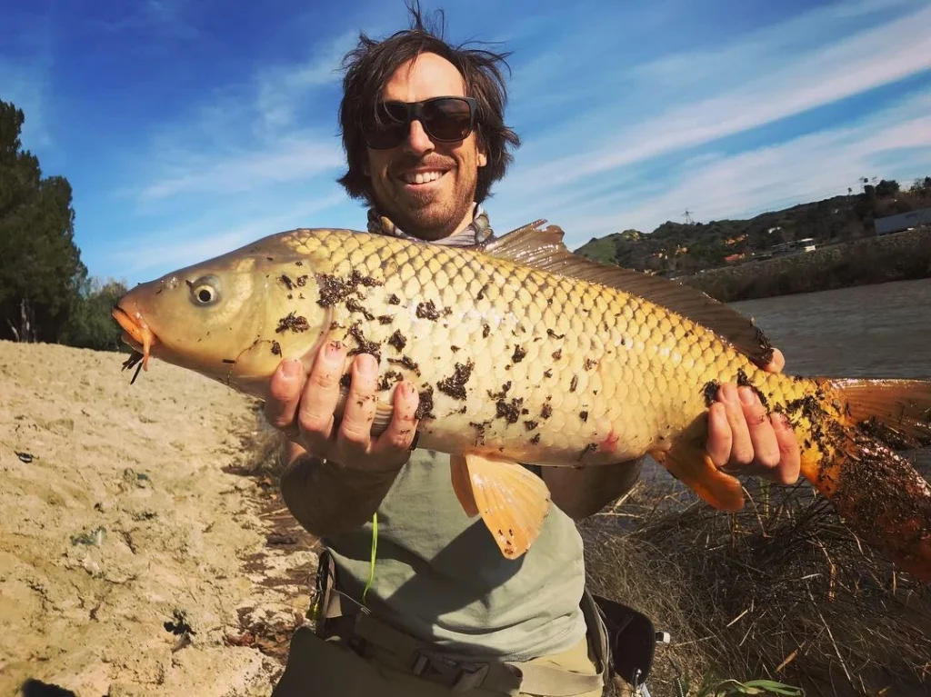 Pablo Signori holding a large carp while fly fishing on a riverbank