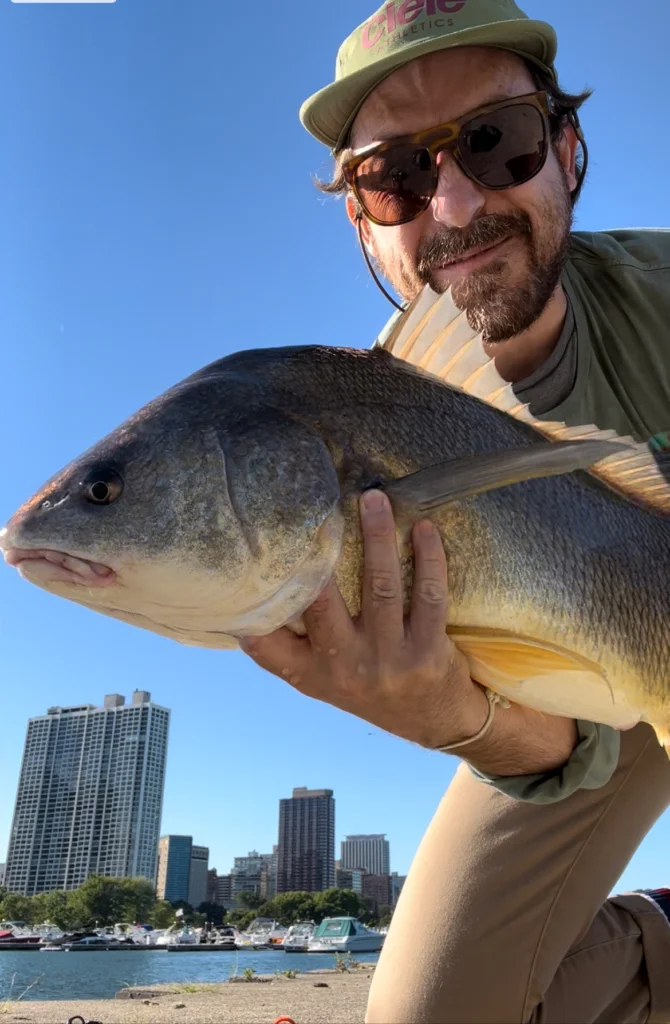 Pablo Signori holding a large fish while fly fishing near a coastal city skyline