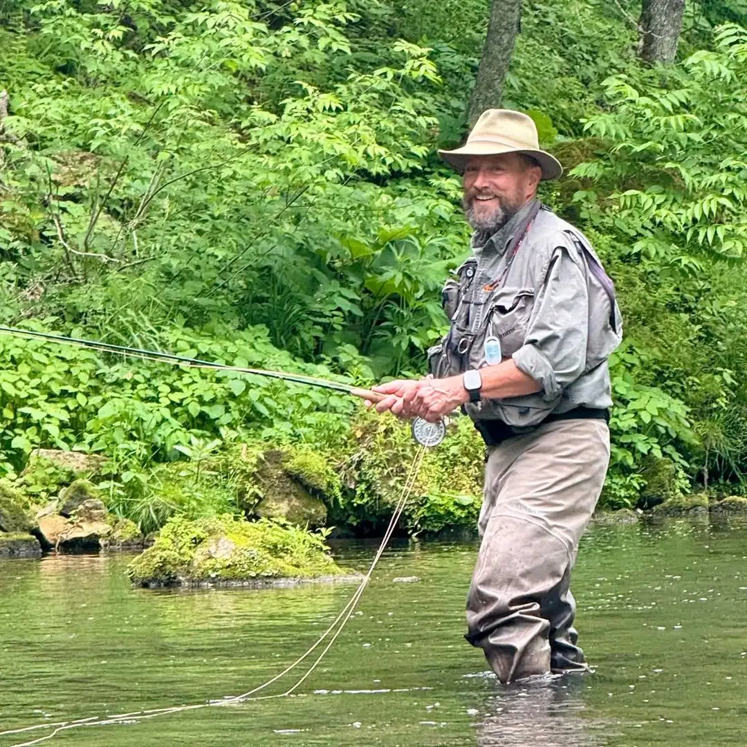 angler fishing a small driftless stream with lush vegetation and clear water