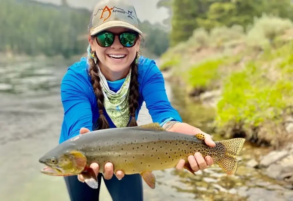 Maggie Heumann holding a trout while fly fishing in a river highlighting trout feeding behavior and aquatic insect patterns