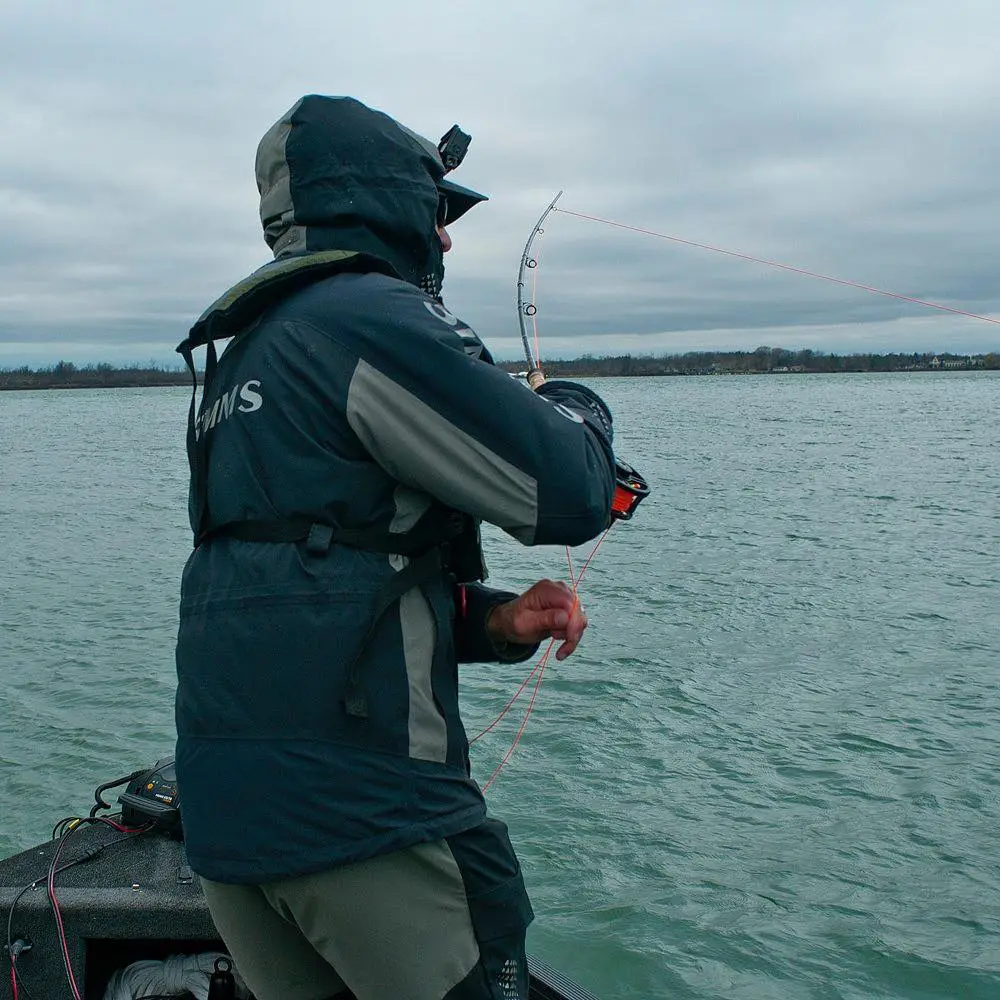 Angler fighting a musky with a deep bend in the fly rod while stripping line from a boat
