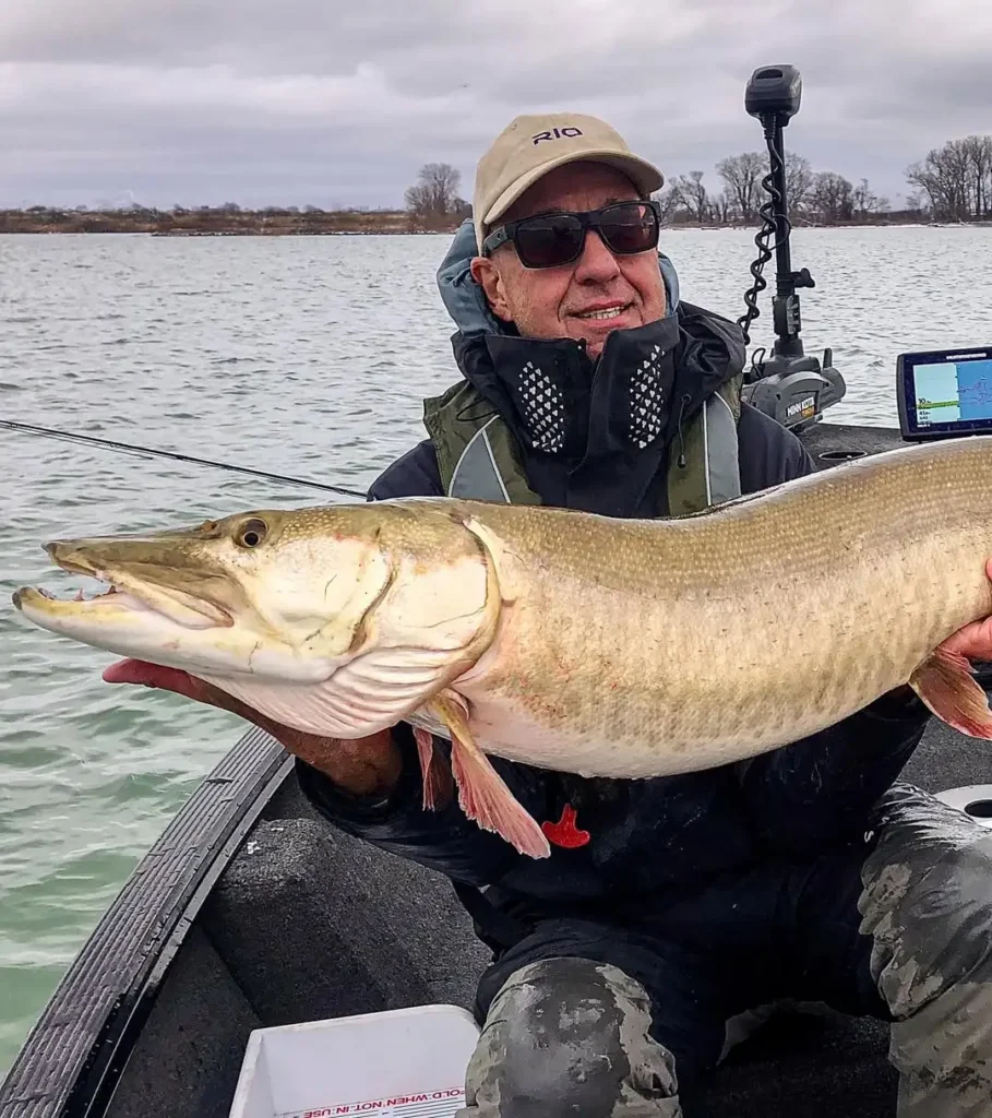 Rick Kustich holding a large musky on a boat after a successful fly catch